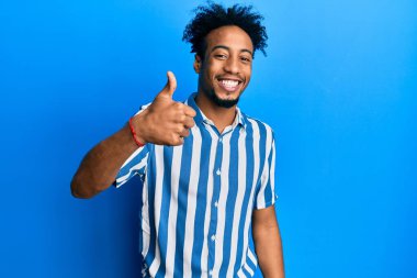Sakallı, sıradan çizgili tişörtlü, mutlu bir şekilde el hareketi yapan Afrikalı genç bir Amerikalı. Kameraya bakıp başarıyı gösteren ifade. 