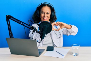 Radyo stüdyosunda çalışan güzel, orta yaşlı bir doktor. Sevgiyle gülümseyen. Elleriyle kalp sembolü ve şekli gösteren. romantik kavram. 