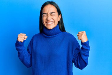 Genç Asyalı kadın, sıradan bir kazak giyiyor. Çok mutlu ve heyecanlı. Kolları havada, gülümseyen ve başarı için çığlık atan kazanan bir jest yapıyor. kutlama konsepti. 