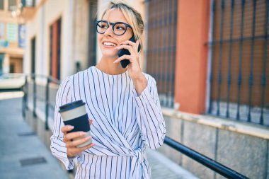 Sarışın iş kadını akıllı telefondan konuşuyor ve şehirde kahve içiyor..