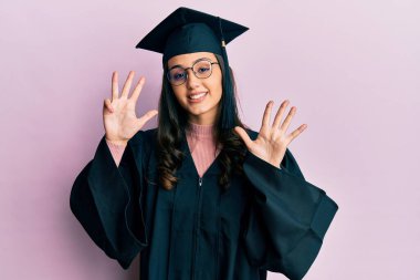 Mezuniyet şapkası ve tören cübbesi takan genç İspanyol kadın dokuz numarayı gösterip işaret ederken kendine güvenen ve mutlu bir şekilde gülümsüyor.. 