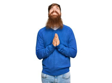 Genç İrlandalı kızıl elbiseli bir adam elleri bağlı yalvarıyor ve dua ediyor. Yüzünde umut ifadesi var. Çok duygusal ve endişeli. Yalvarıyor. 