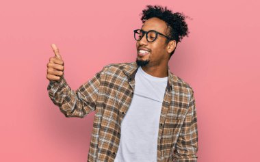 Sakallı, sıradan giyinmiş, gözlüklü, gururlu, gülümseyen ve baş parmak hareketi yapan Afrikalı genç bir Amerikalı. 