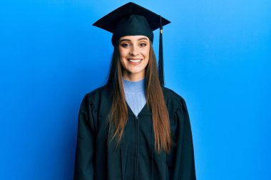 Mezuniyet şapkası ve seremoni cübbesi takan güzel esmer bir kadın. Yüzünde mutlu ve havalı bir gülümseme var. şanslı kişi. 