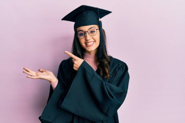 Mezuniyet şapkası ve tören cübbesi giyen genç İspanyol kadın kameraya hayret ediyor ve gülümsüyor.. 