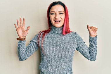 Gündelik giysiler giyen genç beyaz kadın altı numarayı gösterip işaret ederken kendinden emin ve mutlu gülümsüyor.. 