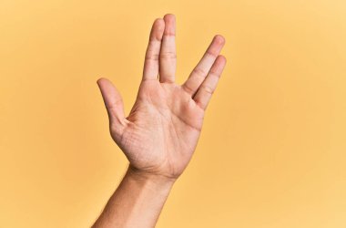 Beyaz adamın kolu ve eli sarı izole arka planda Vulkan selamı veriyor, avuç ve parmaklarını gösteriyor, ucube kültürü sergiliyor. 