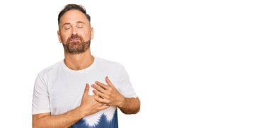 Yakışıklı, orta yaşlı, günlük kravat boyası tişörtü giyen, elleri göğsünde, gözleri kapalı ve yüzünde minnet ifadesi olan bir adam. sağlık kavramı. 