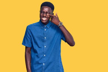 Genç Afro-Amerikan adam, günlük kıyafetler giyip, el ve burunla işaret ederek, neşeyle gülümsüyor. güzellik konsepti 