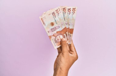 İspanyol el, izole edilmiş pembe arka planda 10 Kolombiya pezosu tutuyor..