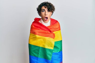 Gökkuşağı lgbtq bayrağına sarılı kadın makyajı yapan genç adam şaşkınlık ve şaşkınlık dolu ifade, korku ve heyecan dolu yüz ifadeleriyle dehşete düşmüş ve şok olmuştu.. 