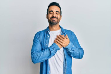 Gündelik kıyafetler giyen genç İspanyol adam elleri göğsünde gülümsüyor, gözleri kapalı ve yüzünde minnet ifadesi var. sağlık kavramı. 