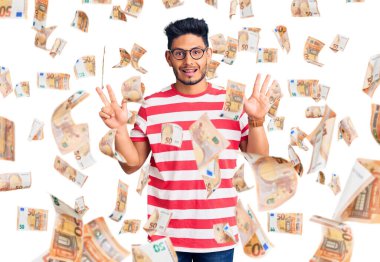 Yakışıklı Latin Amerikalı gündelik kıyafetler ve gözlük takan genç adam sekiz numarayı gösterip işaret ederken kendinden emin ve mutlu gülümsüyor..