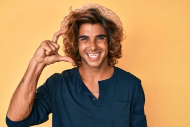 Yaz şapkası takan, gülümseyen, kendine güvenen, el hareketi yapan, parmaklarıyla işaret yapan ve kameraya bakan İspanyol bir genç. ölçüm kavramı. 