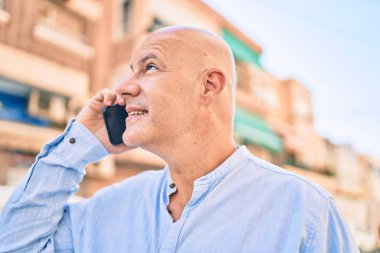 Orta yaşlı kel adam gülümsüyor. Şehirdeki akıllı telefondan mutlu mesut konuşuyor..