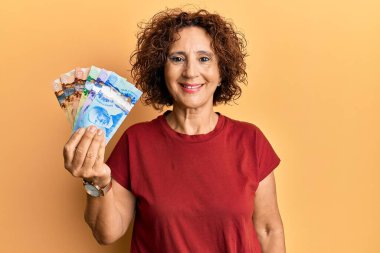 Güzel, orta yaşlı olgun bir kadın elinde Kanada doları tutuyor. Pozitif ve mutlu görünüyor. Kendine güvenen bir gülümsemeyle dişlerini gösteriyor. 