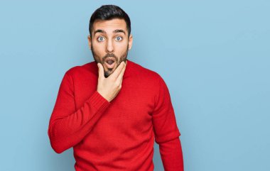 Gündelik kıyafetler giyen genç İspanyol adam, elleri çenesinde, inanamama, şaşkınlık ve şaşkınlık dolu bir ifade takınıyor. 