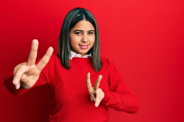 Gündelik kıyafetler giyen genç Latin kadın kameraya bakıp zafer işareti yapıyor. İki numara.. 