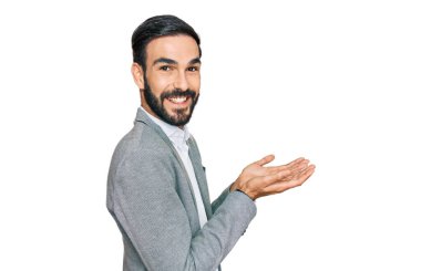 İş kıyafetleri giymiş genç İspanyol bir adam avuç içi açık bir şekilde fotokopi alanını gösteriyor, reklam sunuyor mutlu bir şekilde gülümsüyor. 