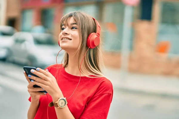 白人のティーンエイジャーの女の子笑顔幸せな使用してスマートフォンやヘッドフォンで街 — ストック写真