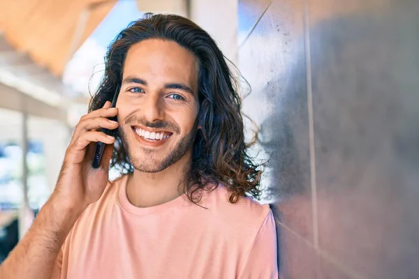 若いヒスパニック系の男笑顔幸せな話でスマートフォンの壁にもたれて — ストック写真