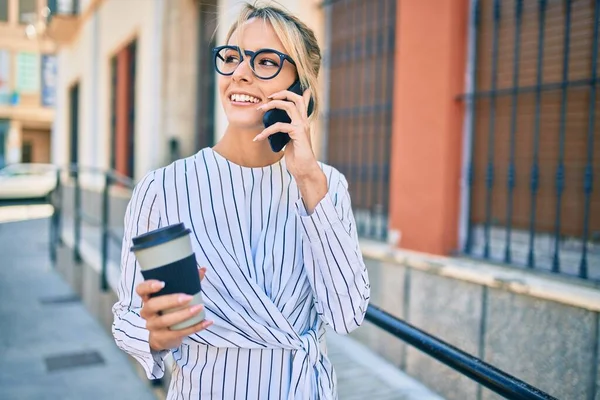 Sarışın iş kadını akıllı telefondan konuşuyor ve şehirde kahve içiyor..