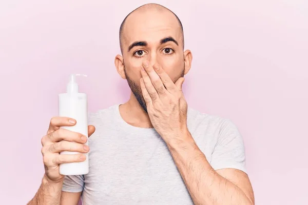 Jovem Careca Bonito Segurando Garrafa Creme Loção Cobrindo Boca Com — Fotografia de Stock