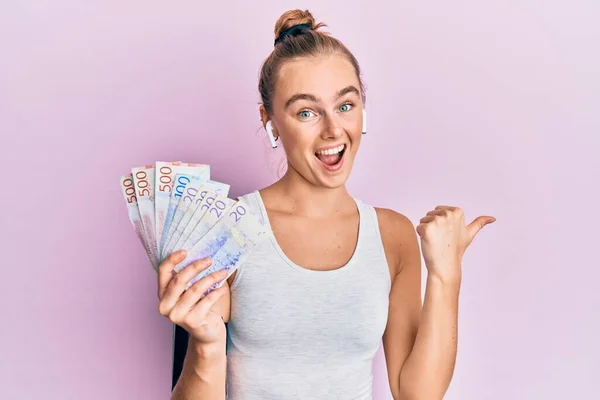 Beautiful Blonde Sport Woman Holding Swedish Krona Banknotes Pointing Thumb — Stock Photo, Image