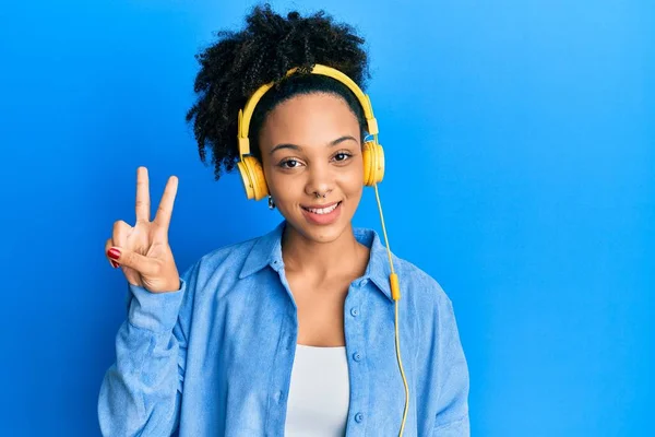 年轻的非洲裔美国女孩 一边用耳机听音乐 一边高兴地微笑着 一边在镜头前眨眼示意胜利 第二点 — 图库照片