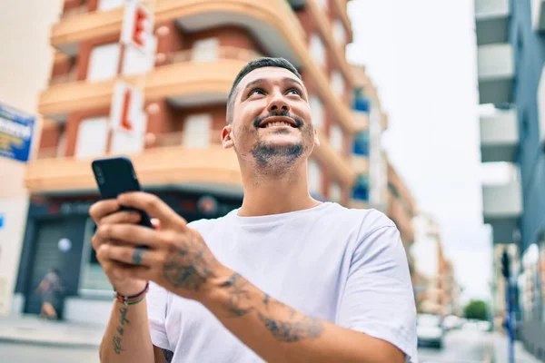 若いヒスパニック系の男が街の通りでスマートフォンを使って笑顔で幸せ — ストック写真