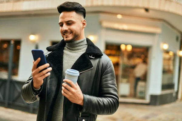 Genç Arap adam akıllı telefon kullanıyor ve şehirde kahve içiyor..