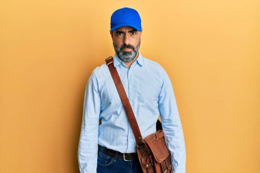 Orta yaşlı, sakallı, gri saçlı, kurye şapkalı, kuşkucu ve sinirli bir adam. Sorun yüzünden surat asıyor. negatif kişi. 