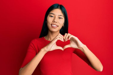 Gündelik kıyafetler giyen, aşık gülümseyen, elleriyle kalp sembolü yapan genç Çinli bir kadın. romantik kavram. 