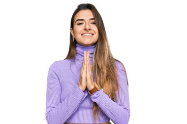 Gündelik giysiler giyen genç İspanyol kadın elleriyle dua ediyor af diliyor kendinden emin bir şekilde gülümseyerek.. 