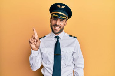 Uçak pilotu üniforması giyen yakışıklı İspanyol adam başarılı bir fikirle işaret ediyor. Heyecanlı ve mutlu. Bir numara.. 