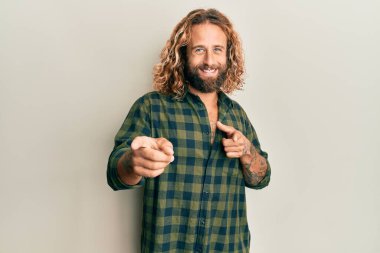 Sakallı, uzun saçlı, sıradan kıyafetler giyen, mutlu ve komik yüzüyle kamerayı işaret eden yakışıklı bir adam. iyi enerji ve titreşimler. 