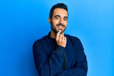 Gündelik giysiler giyen genç İspanyol adam kameraya kollarını kavuşturup çenesine dokunarak gülümsüyor. Olumlu düşünmek. 