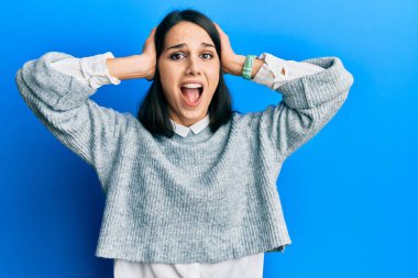 Genç İspanyol kadın gündelik kıyafetler giyiyor çılgın ve elleri başının üstünde korkmuş, korkmuş ve ağzı açık şoktan şaşırmış. 