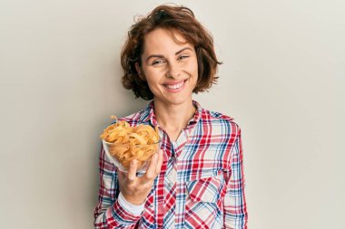 Elinde İtalyan makarnası olan genç esmer kadın pozitif ve mutlu görünüyor ve kendine güvenen bir gülümsemeyle dişlerini gösteriyor. 