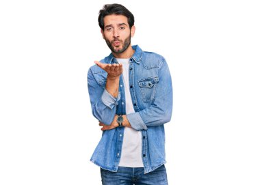 Gündelik giysiler giymiş genç İspanyol bir adam kameraya bakıp havada bir öpücük savuruyor ve sevimli ve seksi oluyor. aşk ifadesi. 