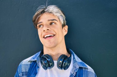 Şehirde kulaklık takarak mutlu gülümseyen genç İspanyol adam..