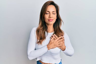 Gündelik kıyafetler giyen, göğsünde elleri olan, yüzünde minnet dolu bir jestle gülümseyen genç Latin bir kadın. sağlık kavramı. 