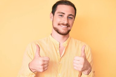 Gündelik kıyafet giyen yakışıklı bir adam. Başarı işareti yapıyor. Elleriyle olumlu jest yapıyor. Neşeli ifade ve kazanan jest. 