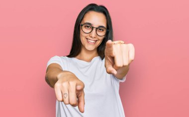 Young hispanic woman wearing casual white t shirt pointing to you and the camera with fingers, smiling positive and cheerful 