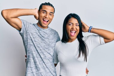 Genç Latin çift gündelik kıyafetler giyiyor çılgın ve elleri başının üstünde korkmuş, korkmuş ve ağzı açık şoktan şaşırmış. 