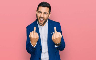 Young hispanic man wearing business jacket showing middle finger doing fuck you bad expression, provocation and rude attitude. screaming excited 