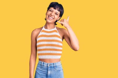 Kısa saçlı esmer bir kadın, günlük kıyafetler giyiyor, gülümsüyor telefonla el ve parmak hareketleri yapıyor, telefonda konuşuyor gibi. iletişim kavramları. 