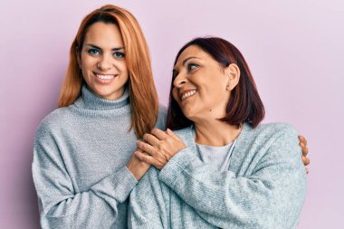İspanyol anne ve kızı mutlu bir şekilde gülümsüyor ve soyutlanmış pembe arka planda duruyorlar..