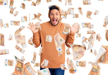 Kış süveteri ve yün şapka giyen yakışıklı Latin Amerikalı genç adam çılgın kutlamalar yapıyor ve kollarını kaldırmış ve gözleri açık bir şekilde heyecanla haykırıyor. Kazanan konsept