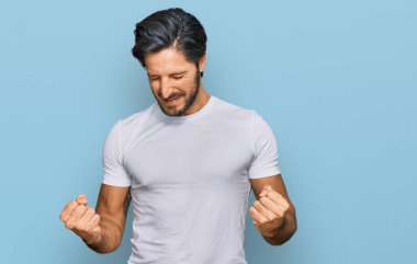 Kolları havada ve gözleri kapalı zaferi kutlayan günlük beyaz tişört giyen İspanyol genç adam. Kazanan konsept. 